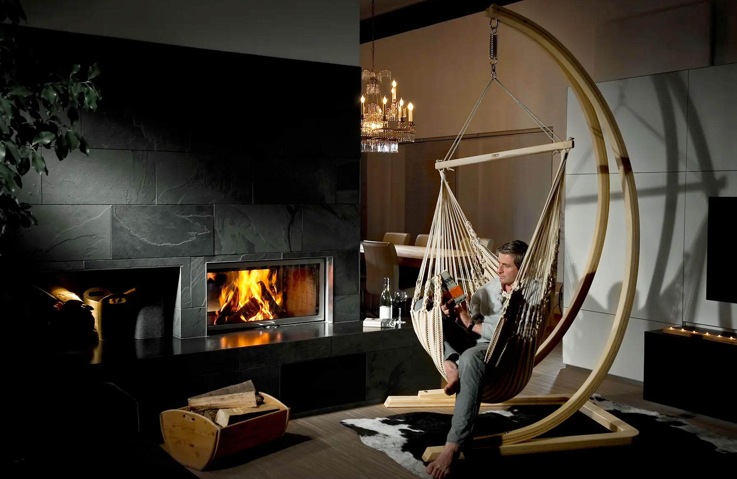 Wohnzimmer mit Feuer im Kachelofen und ein Mann der in der Hängematte sitzt und ein Buch liest
